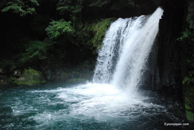 Shokeidaru waterfall flowing beside green trees into the river