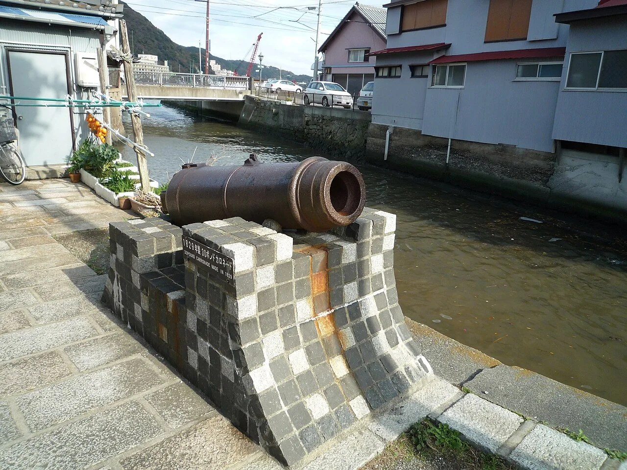 Old cannon beside the canal and buildings on Perry Road in Shimoda